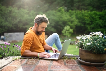 Man enjoying remote work on a laptop in his vibrant garden, illustrating the quality of life and serene outdoor environments offered by new residential projects in Bangalore by Mana Projects.
